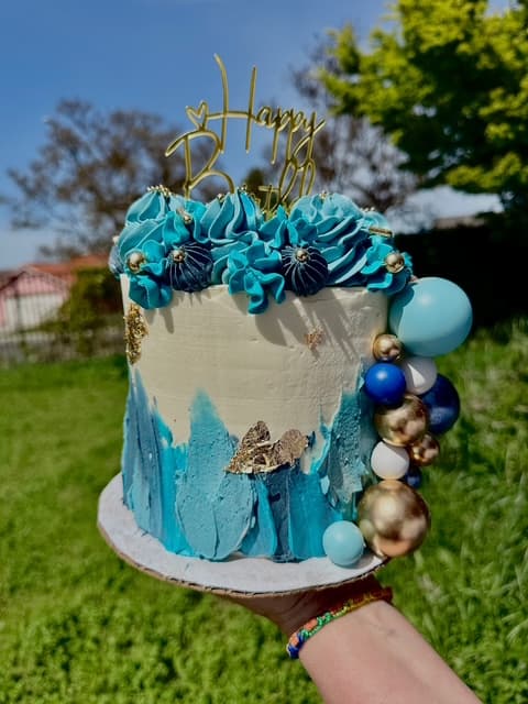 Blue birthday cake with blue frosting, gold accents, balloons, and a Happy 27 topper