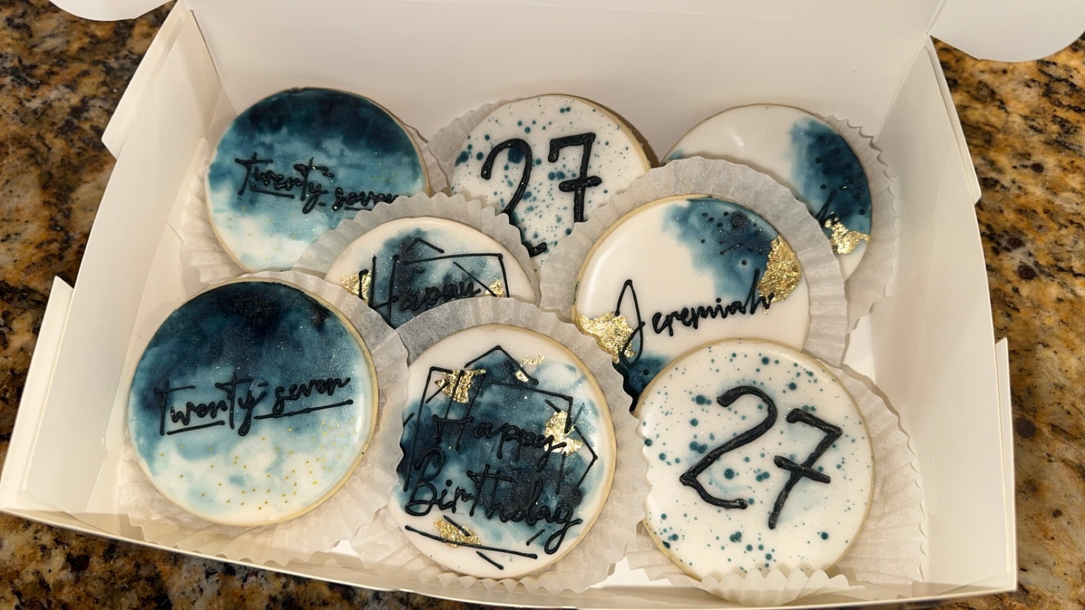 Round blue and white birthday cookies decorated with names, dates, and the number 27