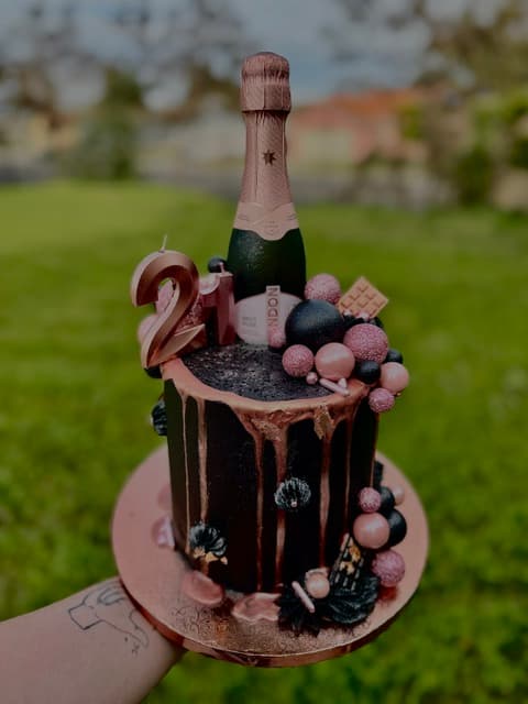 Chocolate 21st birthday cake with pink decorations, a champagne bottle topper, and chocolate drips