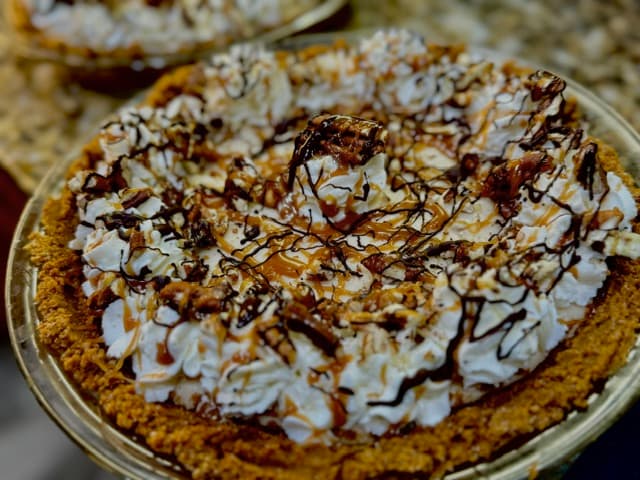 Chocolate and caramel pie topped with whipped cream, nuts, and chocolate drizzle